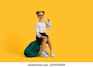 Great Idea. Smart Little Schoolgirl Pointing Finger Up While Sitting On Stack Of Books, Cute Preteen Female Child Having Eureka Moment, Posing Isolated On Yellow Background, Copy Space - Powered by Shutterstock