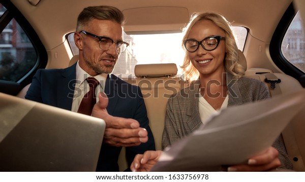 Great job. Two excited business\
people in classic wear analyzing documents and smiling while\
sitting in the car. Business concept. Success.\
Partnership