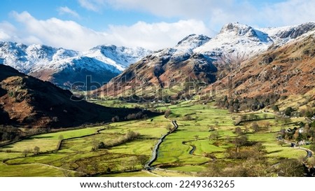 Great Langdale Valley with green pastures on the valley floor with white tipped mountains and fells