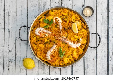 Great mixed seafood and chicken Valencian paella presented in a paella pan with squid, prawns, mussels and chunks of stewed chicken and aioli sauce