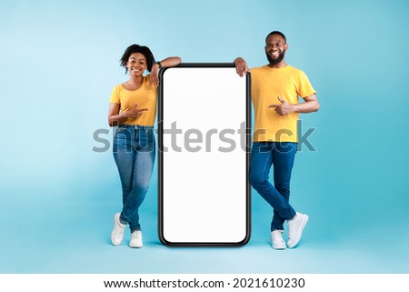 Great mobile app. African American couple pointing at giant smartphone with mockup, promoting application or website, advertising product or service, blue background. Full length Foto stock © 