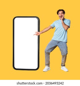 Great Mobile Offer. Excited Guy Pointing Finger At Big White Smart Phone Screen, Emotionally Reacting To New App, Overjoyed Young Male Standing Isolated Over Orange Studio Background, Mock Up - Shutterstock ID 2036493242