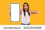 Great Mobile Offer. Excited Lady Pointing Finger At Smartphone In Her Hand, Emotionally Reacting To New App, Overjoyed Millennial Woman Standing Isolated Over Orange Studio Background, Panorama