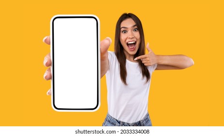Great Mobile Offer. Excited Lady Pointing Finger At Smartphone In Her Hand, Emotionally Reacting To New App, Overjoyed Millennial Woman Standing Isolated Over Orange Studio Background, Panorama - Shutterstock ID 2033334008