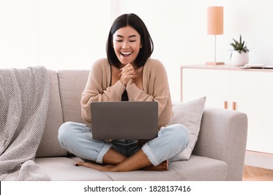 Great News Concept. Portrait Of Emotional Ecstatic Asian Woman Celebrating Online Win Sitting On The Sofa At Home, Using Laptop Computer, Copy Space. Shocked Surprised Female Model Looking At Pc