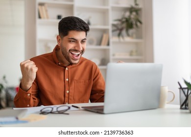 Great News Concept. Portrait of joyful excited guy using pc sitting at desk looking at screen, male raising hands with excitement, ecstatic enthusiastic man shaking clenched fists celebrating success