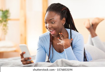Great News. Excited Afro Woman Holding Smartphone Texting Lying In Bed At Home. Selective Focus