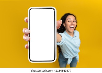 Great Offer. Excited Lady Showing Big White Empty Smartphone Screen Close Up To Camera Recommending Cellular App On Orange Studio Wall, Selective Focus On Hand, Blurred Background. Check This Out