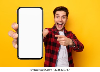 Great Offer. Excited surprised guy holding and pointing finger at big giant cell phone with white screen in hand, promoting application or website, advertising product or service, yellow studio wall - Shutterstock ID 2135539757