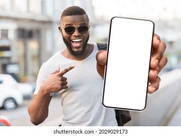 Great Offer. Portrait Of Excited Black Man Standing Outdoors Holding Big Phone With White Blank Screen In Hand, Showing Close To Camera Pointing At Device. Gadget With Empty Free Space For Mock Up