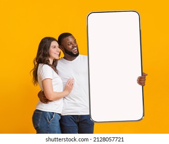 Great Offer. Portrait of smiling interracial couple hugging and holding big giant cell phone looking at white blank device screen in hand, presenting gadget with free copy space for mock up, ad banner - Shutterstock ID 2128057721