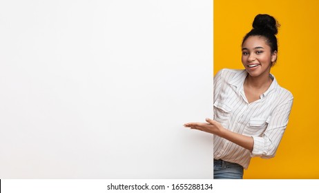 Great Offer. Smiling black woman pointing at white blank advertisement board with open hand, recommending something, panorama