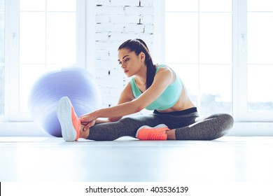 Great progress. Young beautiful woman in sportswear doing stretching while sitting on the floor in front of window at gym - Powered by Shutterstock