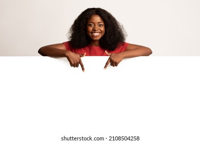 Great Promo. Joyful Black Female Pointing Down At Copy Space On Blank White Advertisement Board With Two Fingers, Happy African American Woman Demonstrating Free Place For Design Or Ad, Mockup - Shutterstock ID 2108504258