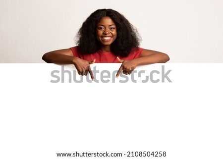Great Promo. Joyful Black Female Pointing Down At Copy Space On Blank White Advertisement Board With Two Fingers, Happy African American Woman Demonstrating Free Place For Design Or Ad, Mockup