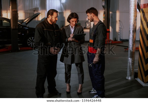 Great team in a auto service center office\
manager and two mechanic man have a conversation in the middle of\
the garage they analyzing\
something