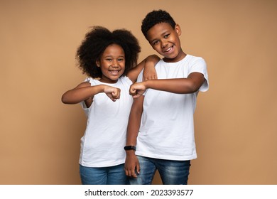 Great team. Portrait of positive brother and sister hugging and bumping with fists with toothy smile, while posing to the camera. Isolated, indoor, studio shot, beige background  - Powered by Shutterstock