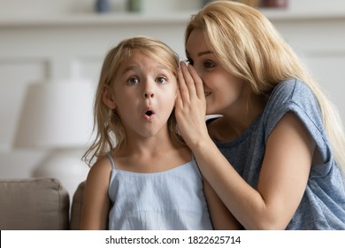 It Is A Great Unknown. Smiling Adult Mom Telling Cute Story As Big Mystery On Ear Of Surprised Little Daughter, Creative Young Nanny Finding Way To Heart Of Small Preschool Child Sharing Funny Secret