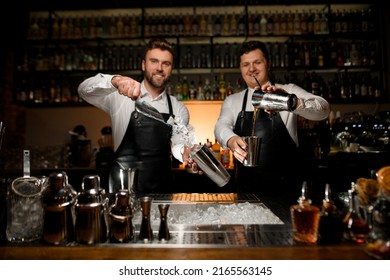 great view of the bar counter with bar accessories behind which two professional male bartenders are preparing cocktails in shakers - Powered by Shutterstock