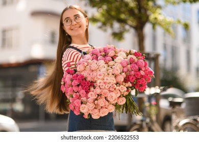 Great view on beautiful lush bouquet of fresh roses of different pink colours which happy smiling woman holds