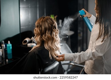 Great view on woman with long curly hair in hair salon and professional hairdresser styling her hairstyle with hairspray. - Powered by Shutterstock