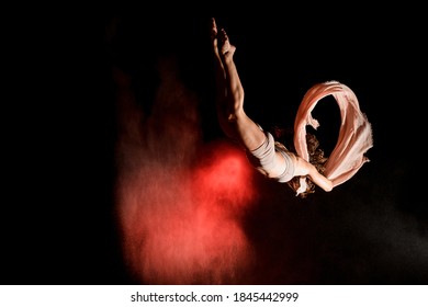 great view of pretty female athlete flying upside down with scarf at dark time and light of searchlight illuminates her - Powered by Shutterstock