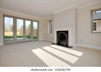 Great Wilbraham, Cambridgeshire, England - March 27 2017: Unfurnished Living Room Within Brand New Home Including Fireplace And Sun Casting Shadows On The Carpet Through Window