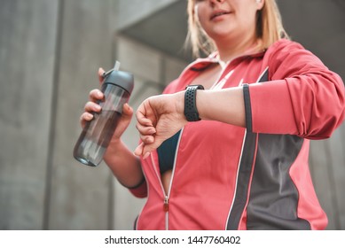 It Was Great Workout. Young Plus Size Woman In Sports Clothing Checking The Pedometer And Holding Bottle Of Water While Standing Outdoors