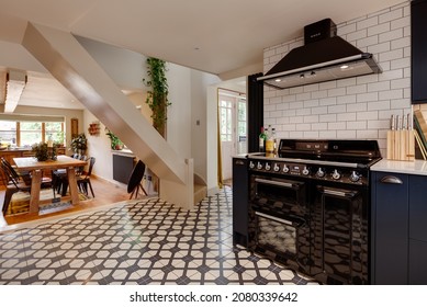 Great Wratting, Suffolk - August 21 2019: Cottage Kitchen With Distinctive Traditional Tile Floor And Striking Dark Coloured Cabinetry With A Range Cooker, Extractor Hood And Dining Room In View