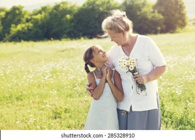 Great-grandmother and granddaughter standing in flower field in sunlight