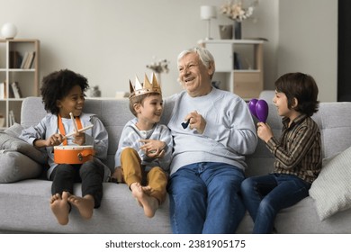 Great-grandpa having fun with three little great-grandchildren, sit together on sofa and play musical instruments, celebrate family holiday, loving grandsons congratulate older relative with birthday - Powered by Shutterstock