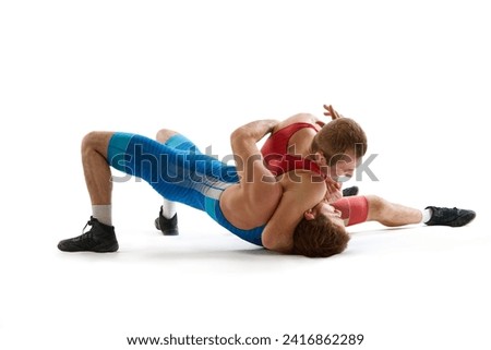 Greco-Roman, freestyle wrestling. Two sportsman, fighting in red and blue uniform in action against white studio background. Concept of fair wrestling, championship, win competition.