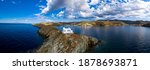 Greece, Kea Tzia island. Drone, aerial panoramic close up view of lighthouse and Agios Nikolaos church on a rocky cape, cloudy blue sky and rippled sea water background. Summer, tourist destination.