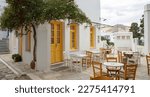 Greece. Tinos island Cyclades. Outdoors traditional cafe with yellow windows at Pyrgos village. Empty chair and table on paved yard