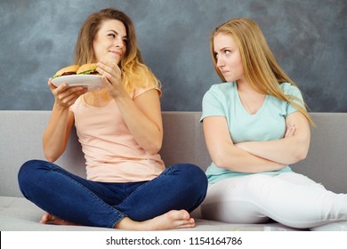 Greed, Envy, Overeating, Food Addiction, Dieting. Young Woman Taking Plate With Burgers Away Of Her Friend 