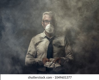 Greedy Business Executive Wearing A Mask And Holding Cash Banknotes: Pollution And Corruption Concept