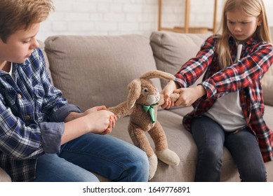 Greedy Children. Boy And Girl Pulling Apart A Toy Not Wanting To Share Sitting On Couch At Home