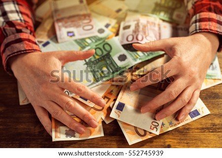 Greedy hands withdrawing pile of euro banknotes cash money on office desk