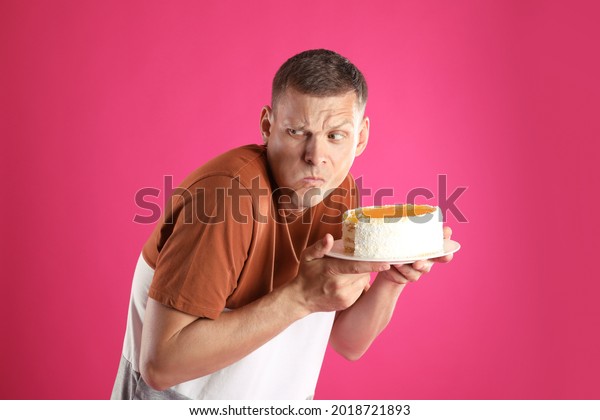 Greedy man\
eating tasty cake on pink\
background