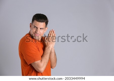Greedy man rubbing hands on grey background, space for text