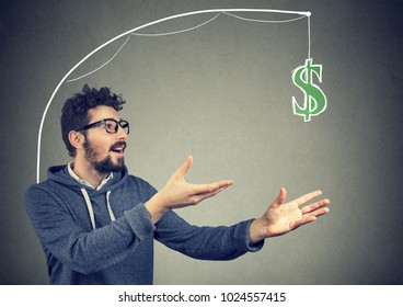 Greedy Young Man Chasing Dollar Bill Money On Gray Background. 