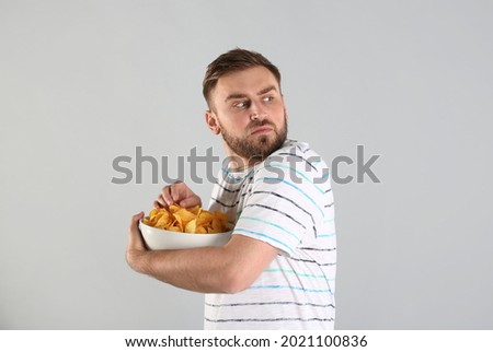 Greedy young man hiding bowl with chips on light grey background Foto stock © 