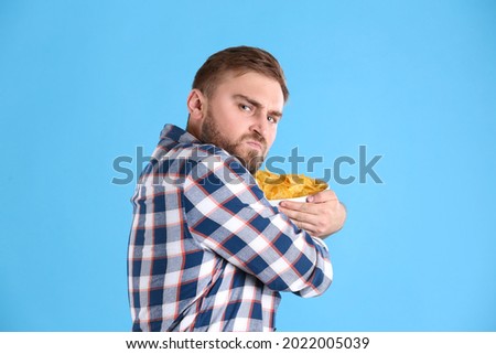 Greedy young man hiding bowl with chips on light blue background Foto stock © 