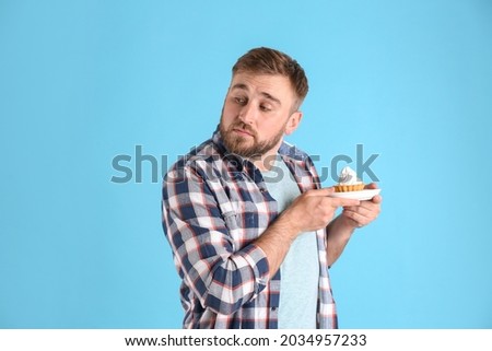 Greedy young man hiding cupcake on light blue background