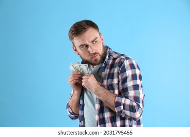 Greedy young man hiding money on light blue background