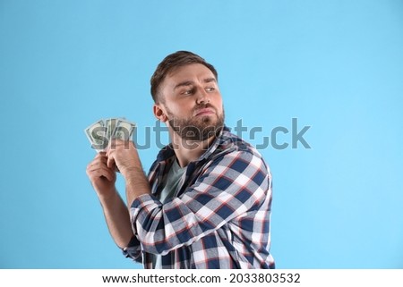 Greedy young man hiding money on light blue background