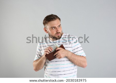 Greedy young man hiding wallet with money on light grey background Foto stock © 