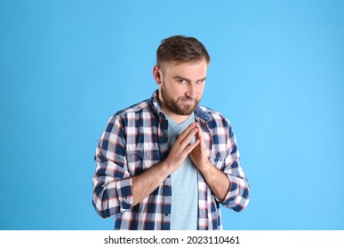 Greedy young man rubbing hands on light blue background