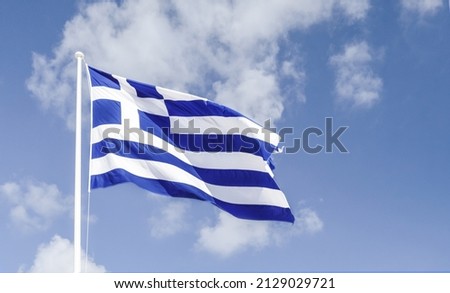The Greek flag flying in the wind against the blue sky.