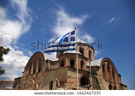 Greek flag waving in the wind with an old byzantine era greek orthodox church in the background